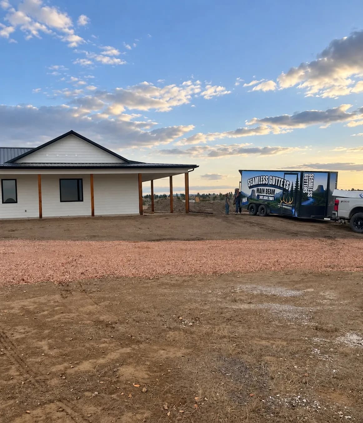 Newly built home with tidy job site, branded trailer and truck parked beside it